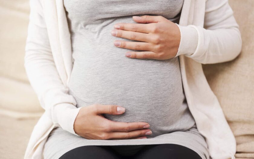 Waiting for a baby. Close-up of young pregnant woman touching her abdomen while sitting on the couch