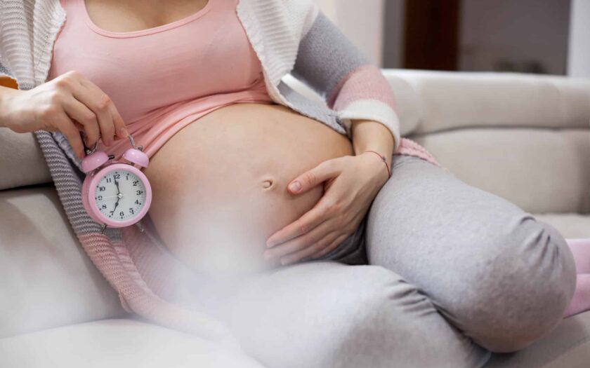 Regnant woman holds hands on belly and looking on an alarm clock.