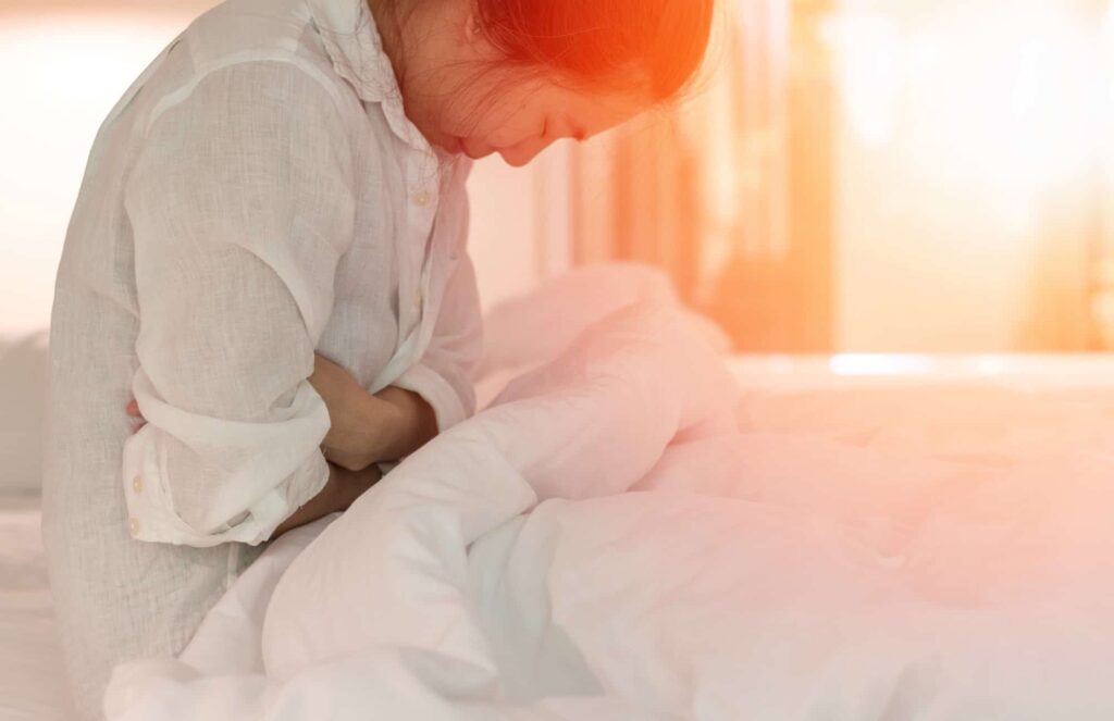 A woman in need of endometriosis treatment is experiencing painful period cramps in bed.