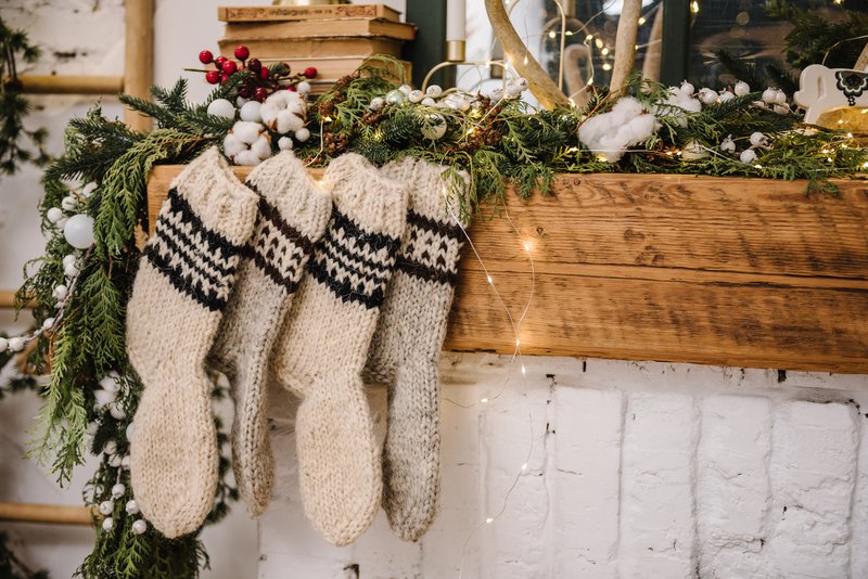 Christmas knitted woolen socks closeup. Decorative fireplace with Christmas stockings, garlands and gifts in stylish room interior. Happy New Year and Merry Christmas.