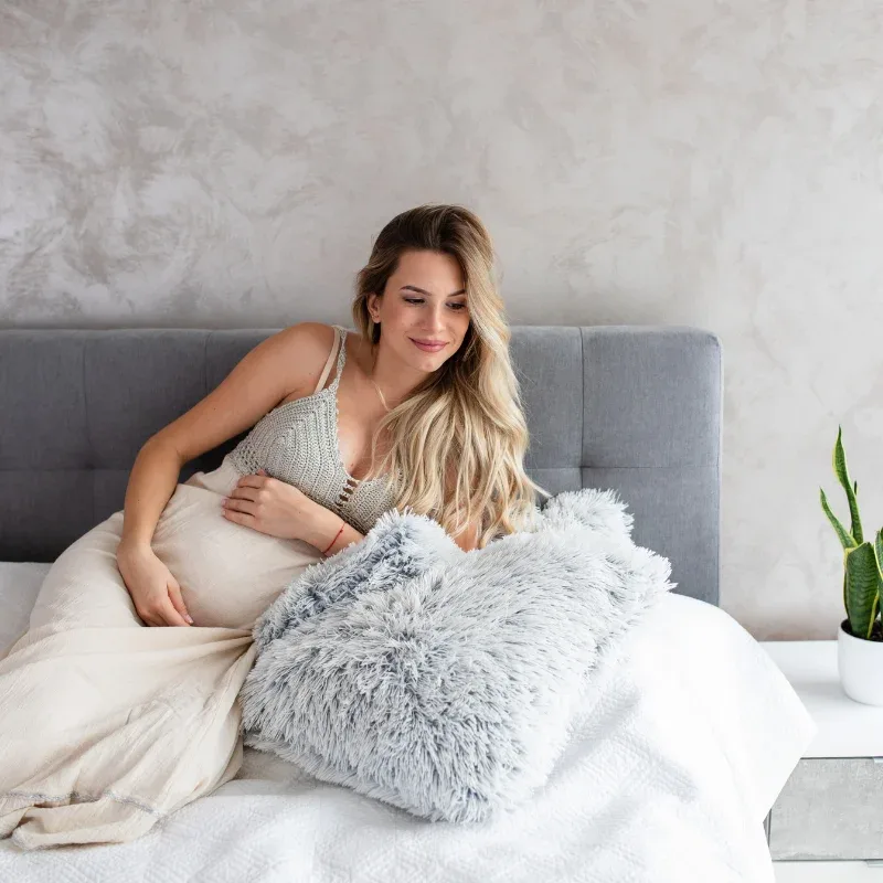 happy blonde pregnant woman lounging on a bed propped up against a fuzzy pillow